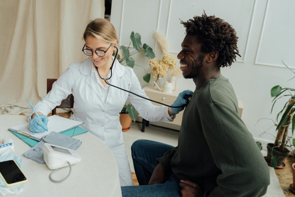 Caucasian female doctor checks black male patient's heart rate with stethoscope in a clinic.
